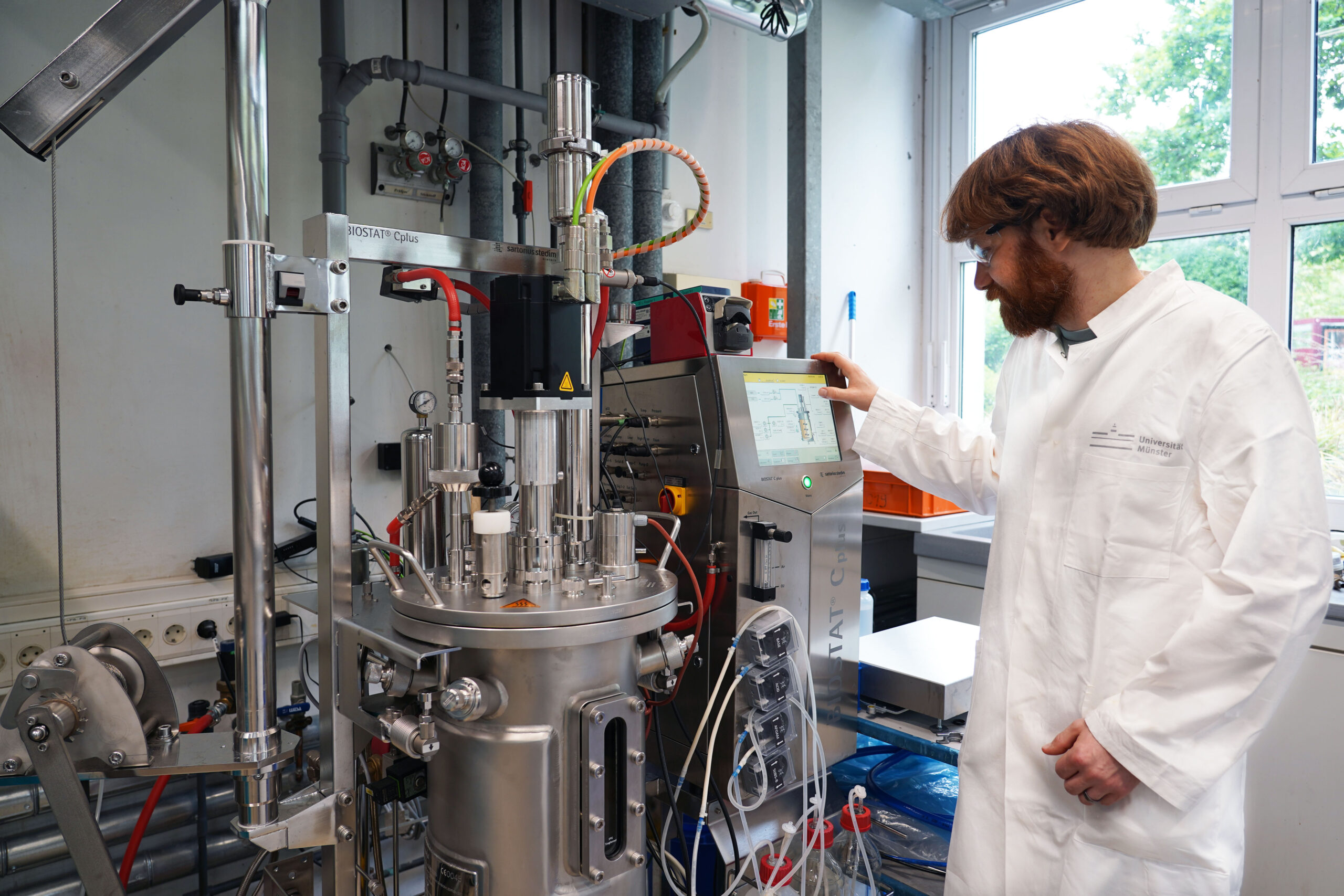 Ein Mann in einem Laborkittel steht in ein Labor und arbeitet an einem Bioreaktor.