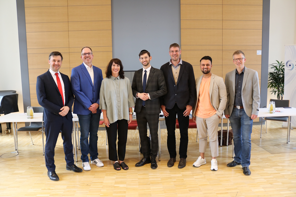 Eine Gruppe Menschen steht in einem Raum und blickt in die Kamera.