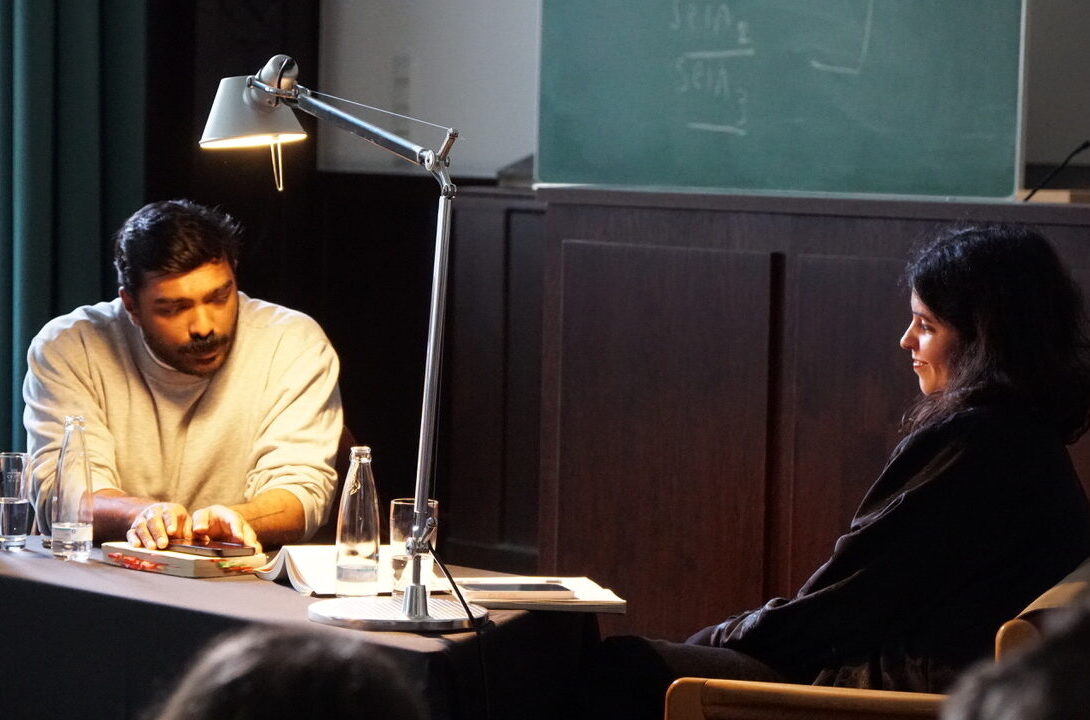 Eine Mann und eine Frau sitzen an einem Tisch. Der Mann liest etwas vor.