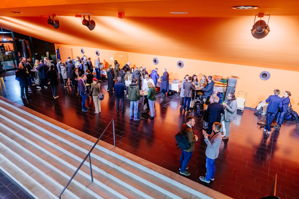 Mehrere Personen stehen in Kleingruppen zusammen in einer großen Aula.