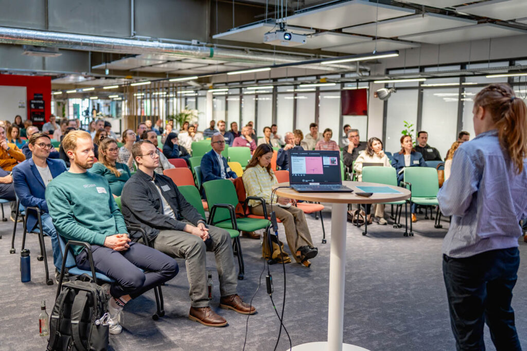 Die Teilnehmenden des Netzwerktreffens kosmos sitzen im Publikum und hören einer Vortragenden zu.