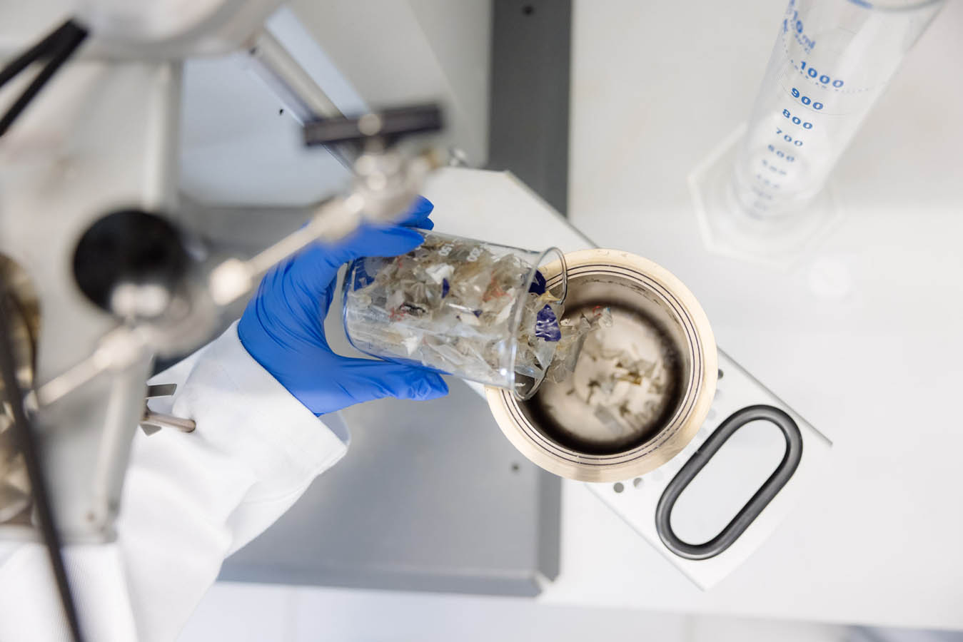 Eine Person schüttet Kunststoffabfälle aus einem Becherglas in ein Metallgerät.