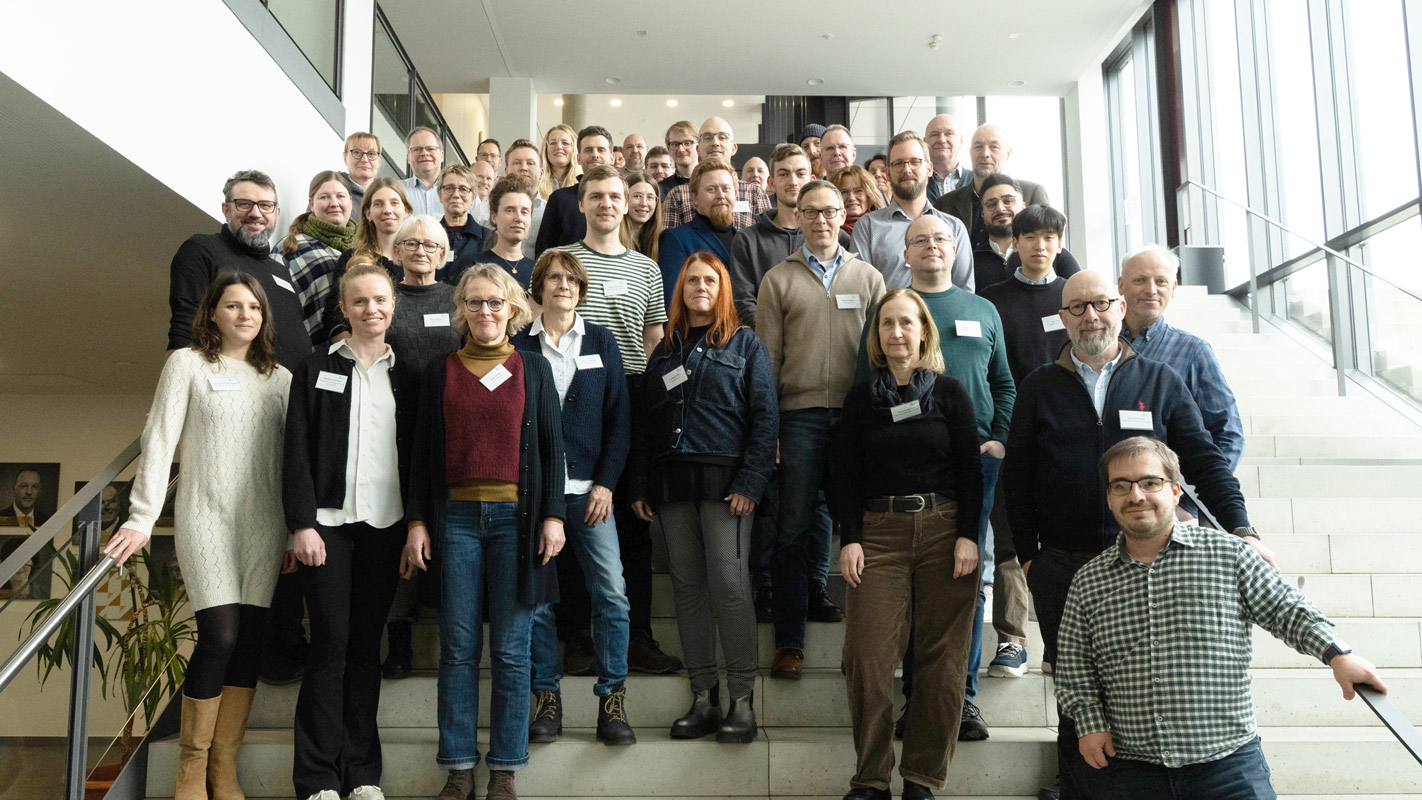Gruppenfoto eines Netzwerktreffens von wasser^plus OWL in Paderborn. Mehrere Personen aus Wissenschaft, Verwaltung und Praxis stehen im Innenraum auf einer Treppe zusammen und blicken in die Kamera.